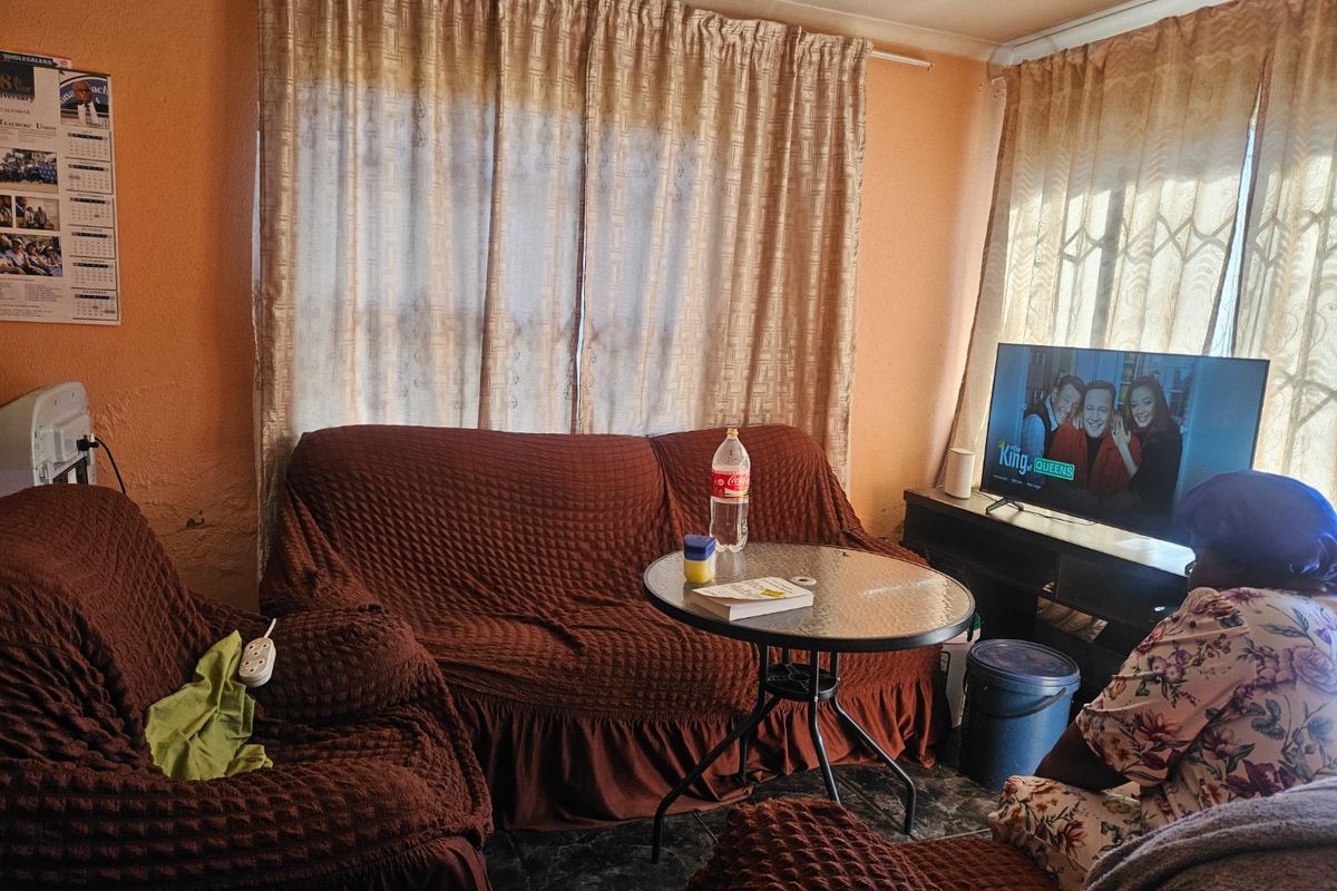 A living room area featuring tiled flooring and natural light through window curtains, requiring cosmetic updates to the wall finishes.