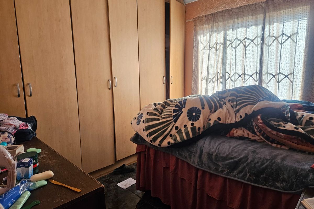 A bedroom featuring built-in wooden cupboards, tiled flooring, and a window fitted with a security gate.
