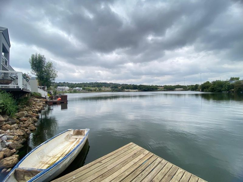 A scenic view of the lake featuring a wooden jetty and a natural rock embankment along the property edge.