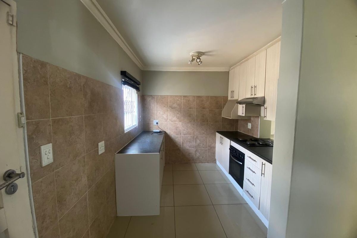 A functional galley-style kitchen featuring built-in cabinetry, a hob, an oven, an extractor fan, and tiled finishes throughout.
