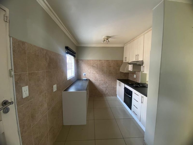 A functional galley-style kitchen featuring built-in cabinetry, a hob, an oven, an extractor fan, and tiled finishes throughout.