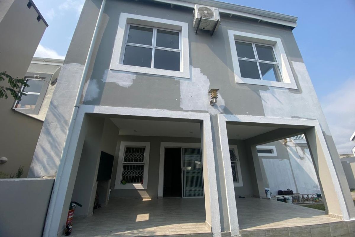 Rear view of the apartment featuring a covered patio area and exterior walls currently undergoing maintenance and repainting.