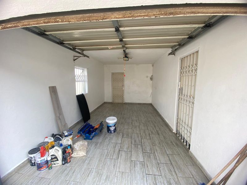 A spacious, empty garage featuring tiled flooring, a sectional door, and secure metal gates, providing a clean and functional storage or parking space.