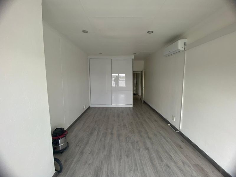 A clean, empty bedroom featuring modern laminate flooring, a built-in sliding wardrobe, and a wall-mounted air conditioning unit.