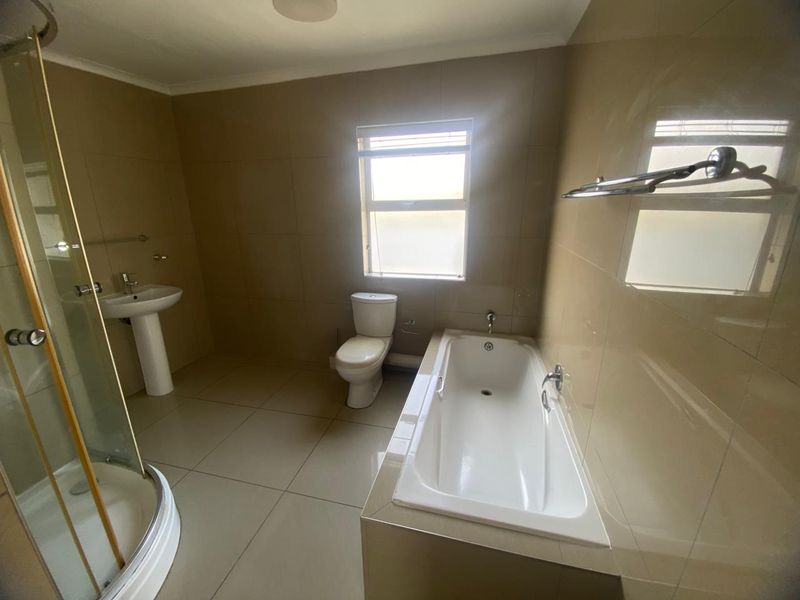 A spacious bathroom featuring a built-in bathtub, separate shower enclosure, pedestal basin, and toilet with neutral wall and floor tiling.