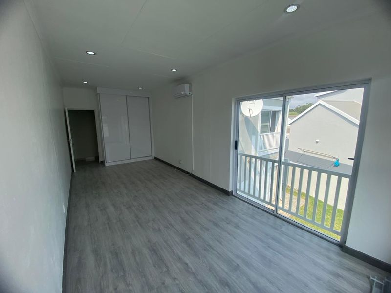 A bright, modern bedroom featuring laminate flooring, built-in wardrobes, recessed lighting, and a sliding glass door leading to a private balcony.