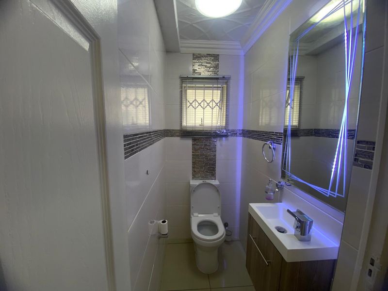 A modern, compact bathroom featuring a vanity basin, toilet, tiled finishes, and an illuminated LED mirror.