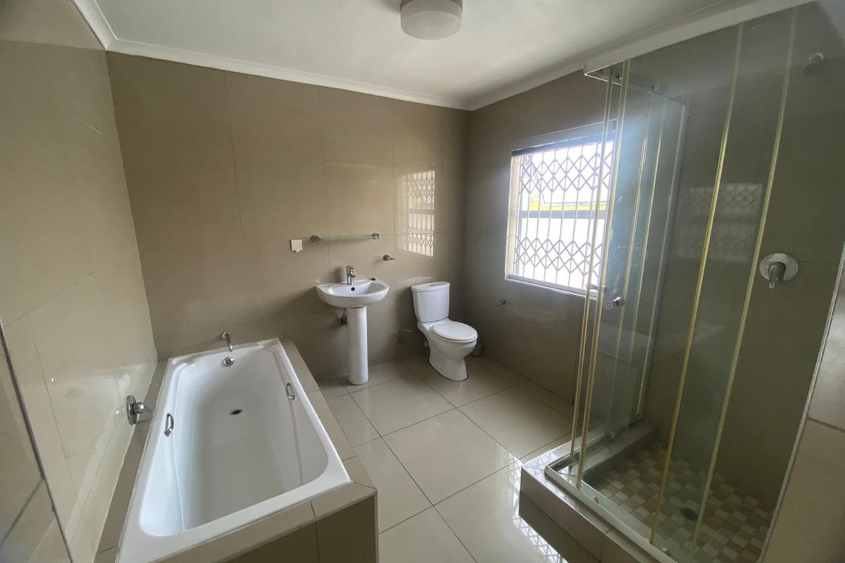 A spacious bathroom featuring a bathtub, separate shower enclosure, pedestal basin, and toilet, finished with neutral wall and floor tiles.