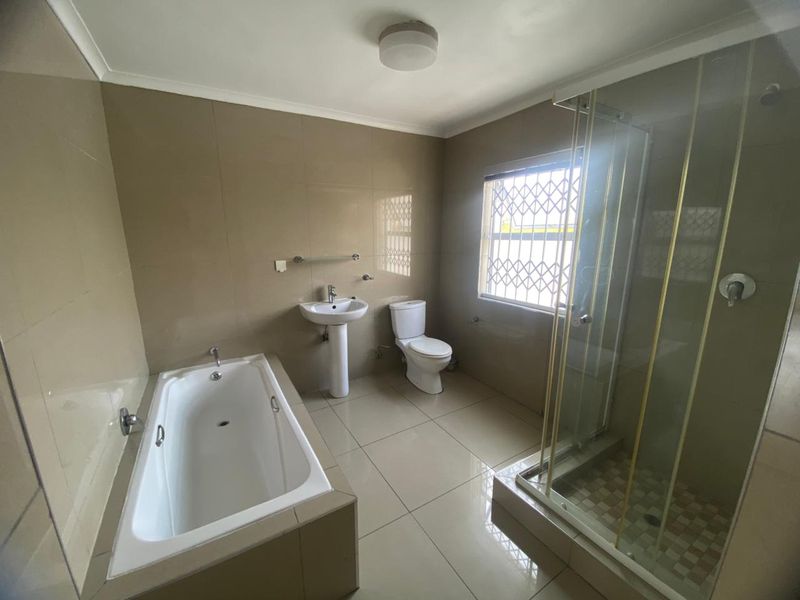 A spacious bathroom featuring a bathtub, separate shower enclosure, pedestal basin, and toilet, finished with neutral wall and floor tiles.