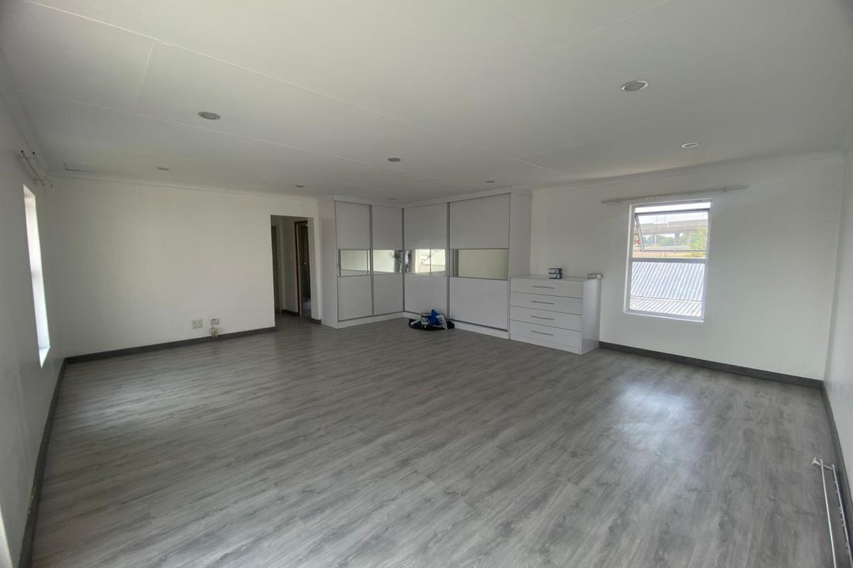 Spacious bedroom featuring modern laminate flooring, recessed downlighting, and extensive built-in cupboard storage with mirrored accents.