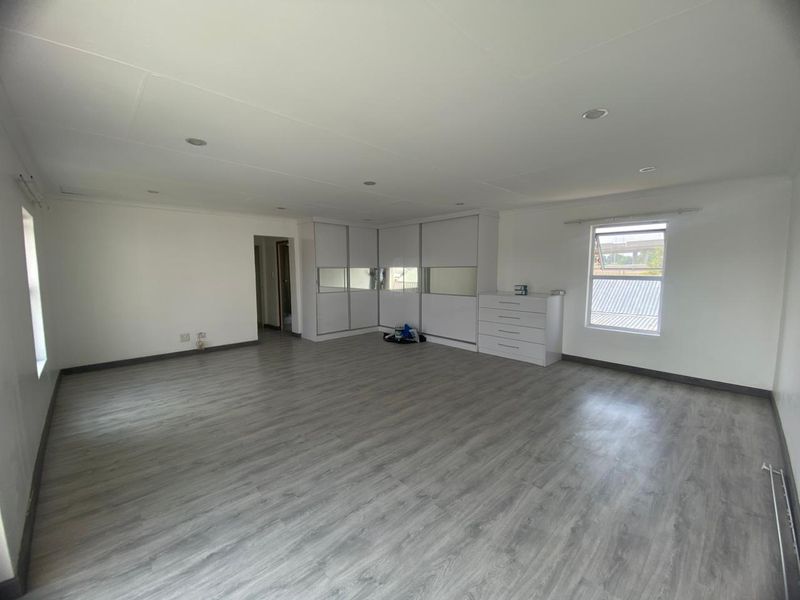 Spacious bedroom featuring modern laminate flooring, recessed downlighting, and extensive built-in cupboard storage with mirrored accents.