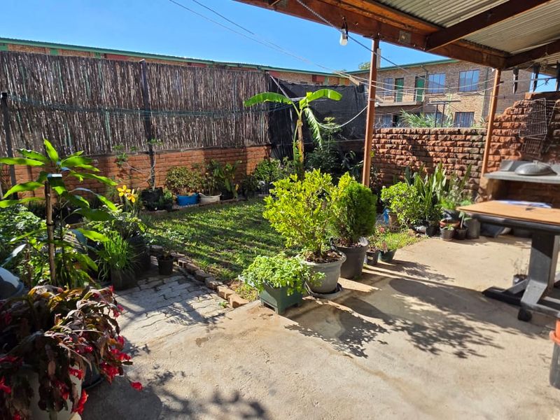 A private rear courtyard featuring a concrete patio, timber pergola, and a built-in brick braai area, enclosed by brick boundary walls.