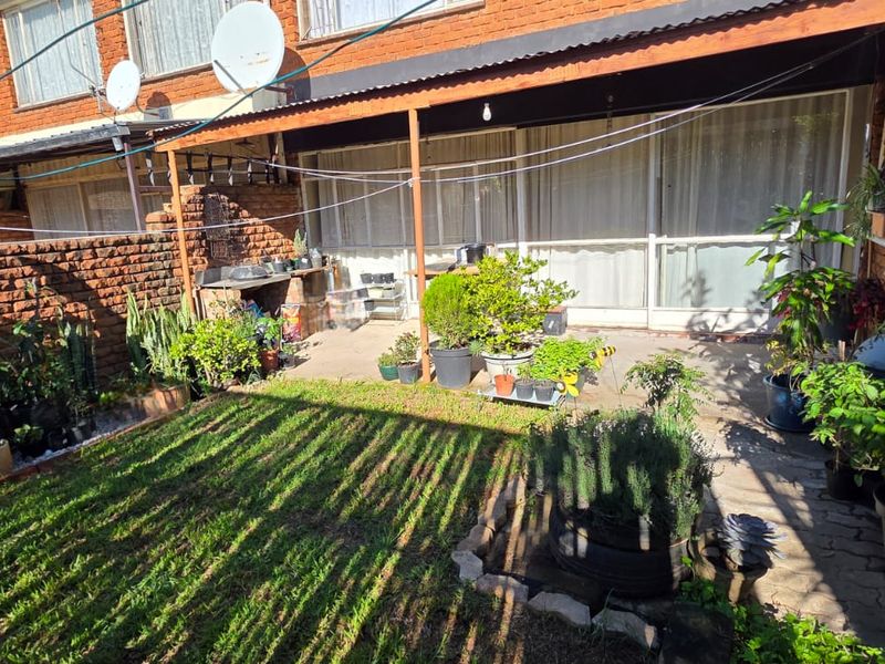 Rear exterior view of the apartment featuring a private garden, paved patio area, and covered outdoor space with sliding door access.