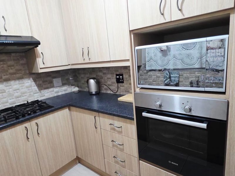 Modern kitchen featuring light wood-finish cabinetry, dark countertops, a gas hob, extractor fan, and integrated oven and microwave appliances.