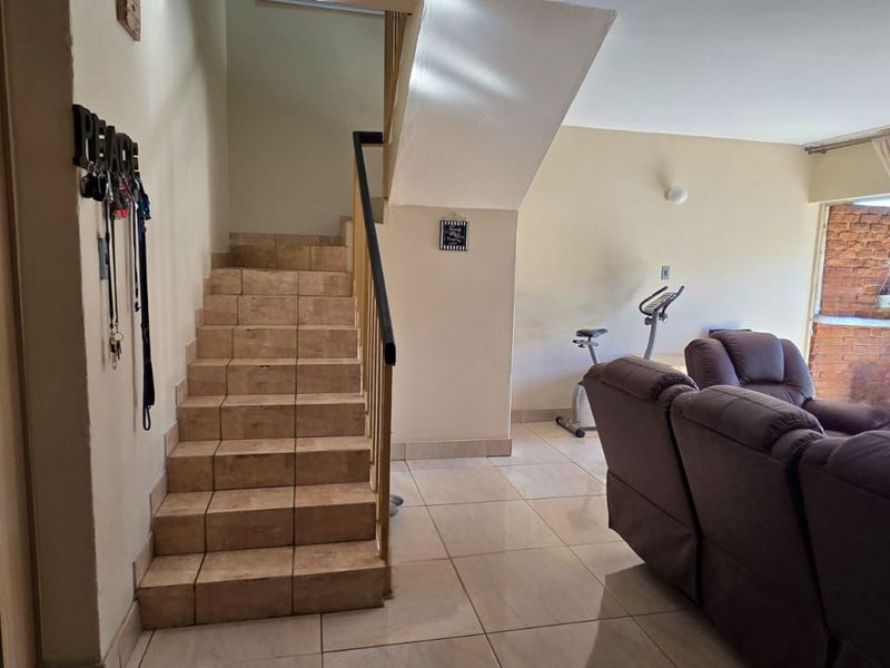 Open plan living area featuring tiled flooring and a staircase with a metal handrail leading to the upper level.