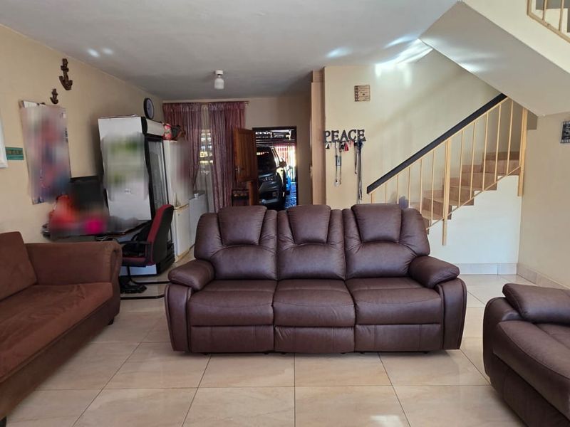 Spacious living room featuring tiled flooring and an integrated staircase with metal railings, providing a functional open-plan layout.