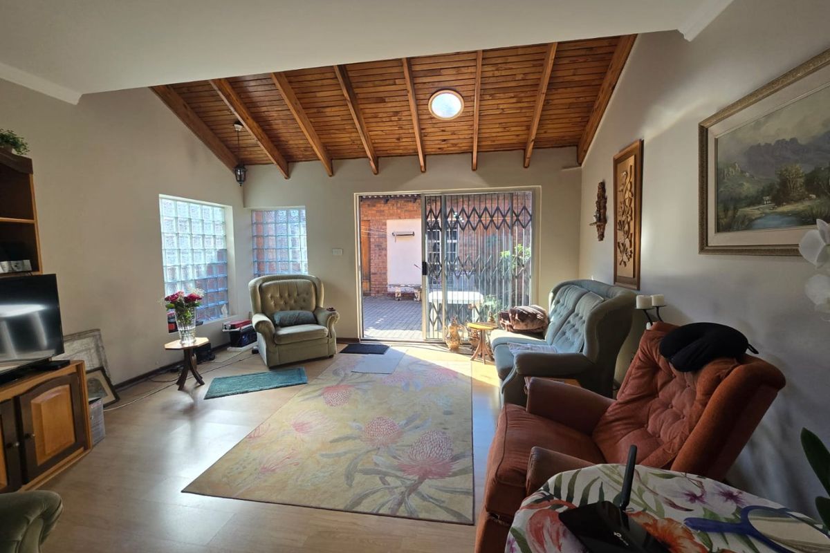 Spacious living room featuring a high exposed timber rafter ceiling, laminate flooring, and glass block windows with direct access to an outdoor patio area.