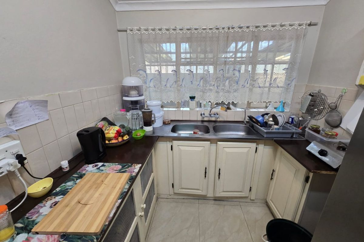 A functional kitchen featuring double stainless steel sinks, tiled splashbacks, laminate countertops, and ample built-in cabinetry with a classic layout.