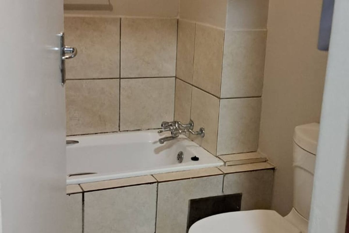 A compact bathroom featuring a bathtub with tiled surround, a standard toilet, and tiled flooring, requiring some maintenance and cosmetic updates.