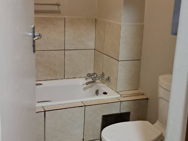 A compact bathroom featuring a bathtub with tiled surround, a standard toilet, and tiled flooring, requiring some maintenance and cosmetic updates.