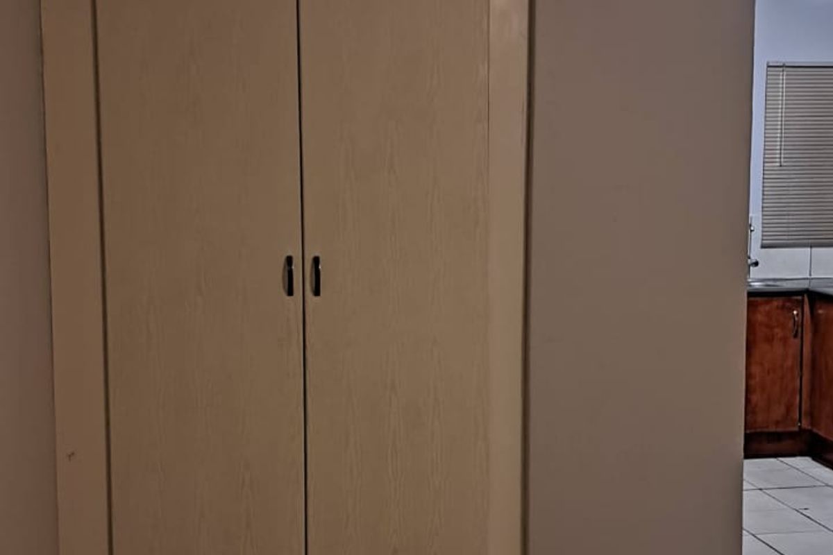 An empty bedroom featuring neutral ceramic floor tiles and a built-in cupboard, offering a blank canvas for potential interior updates.