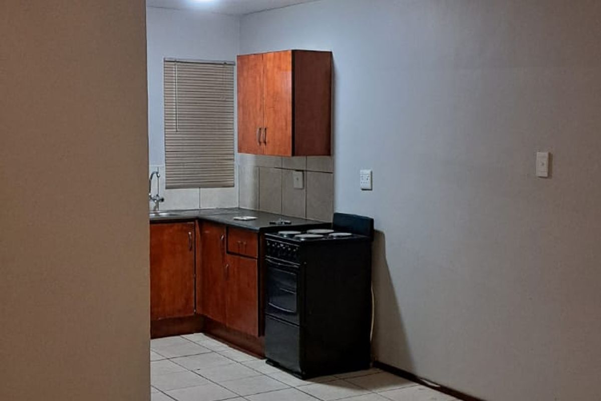 A functional kitchen area featuring tiled flooring, built-in wooden cabinetry, a tiled backsplash, and a freestanding stove.