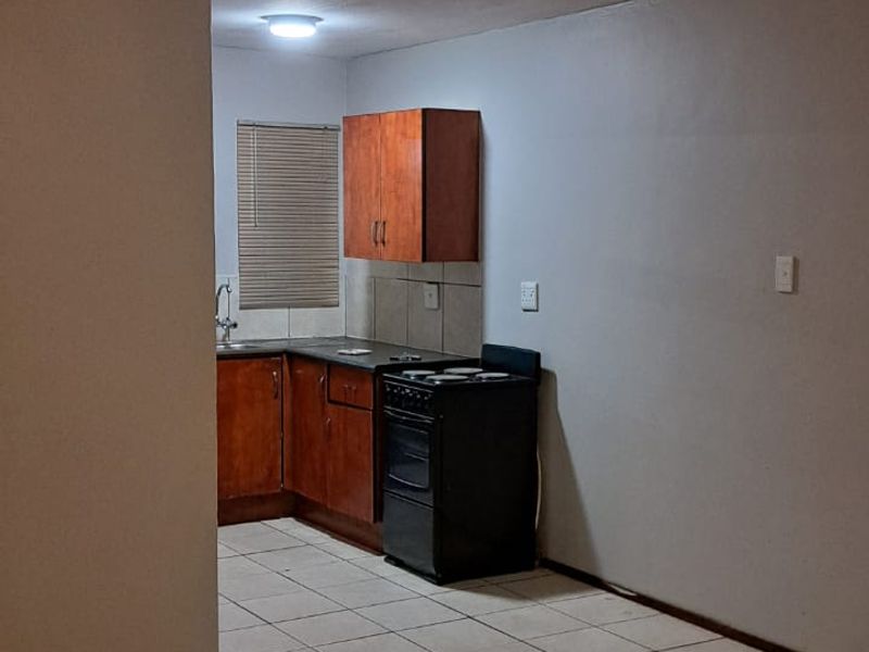 A functional kitchen area featuring tiled flooring, built-in wooden cabinetry, a tiled backsplash, and a freestanding stove.