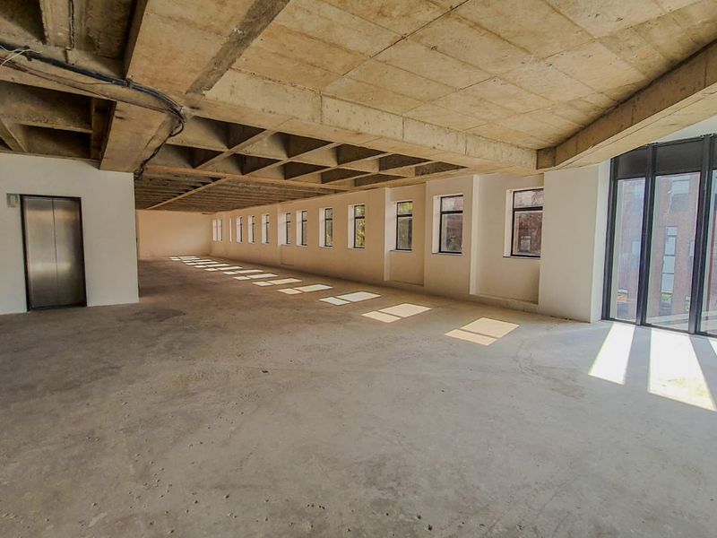 Expansive open-plan commercial office space featuring an exposed concrete waffle ceiling, large windows providing natural light, and direct elevator access.