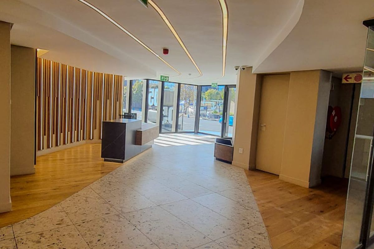 Modern commercial entrance lobby featuring a combination of terrazzo and timber flooring, recessed ceiling lighting, and contemporary timber slat wall paneling.