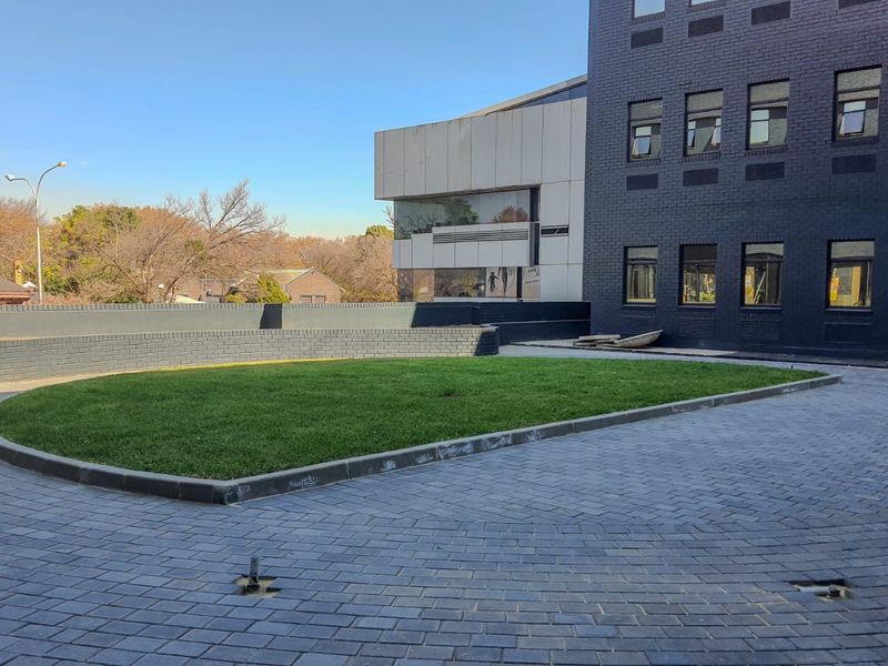 A well-maintained commercial exterior featuring a paved circular driveway, a central lawn area, and a modern multi-story brick and panel facade.