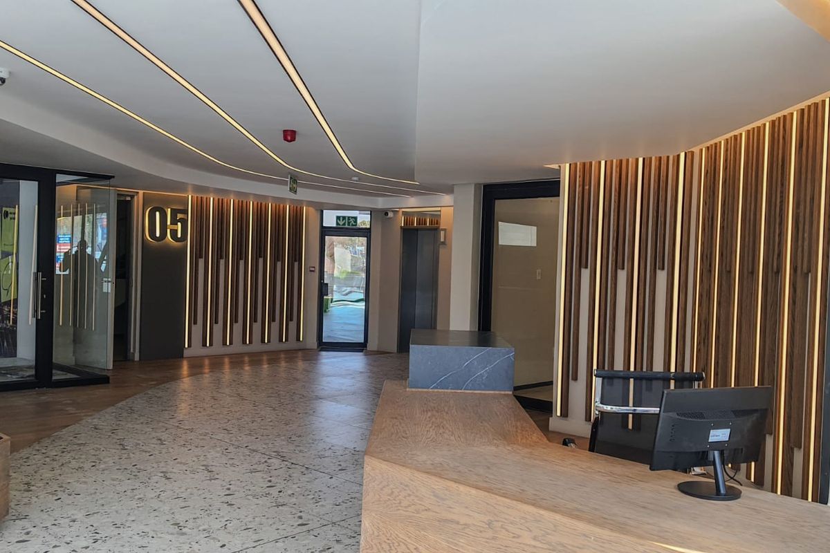 Modern commercial lobby featuring a custom reception desk, elegant timber slat wall paneling with integrated lighting, and high-quality terrazzo flooring.
