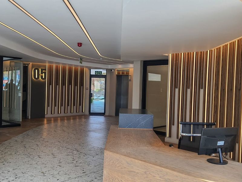 Modern commercial lobby featuring a custom reception desk, elegant timber slat wall paneling with integrated lighting, and high-quality terrazzo flooring.