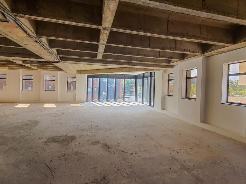 Spacious open-plan commercial area featuring an industrial aesthetic with exposed concrete waffle slab ceilings, large windows, and a full-height glass facade.