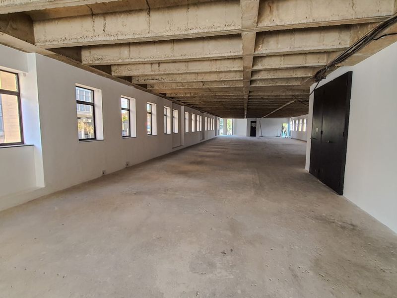 Expansive open-plan commercial space featuring an exposed concrete waffle ceiling, polished concrete floors, and large windows providing ample natural light.