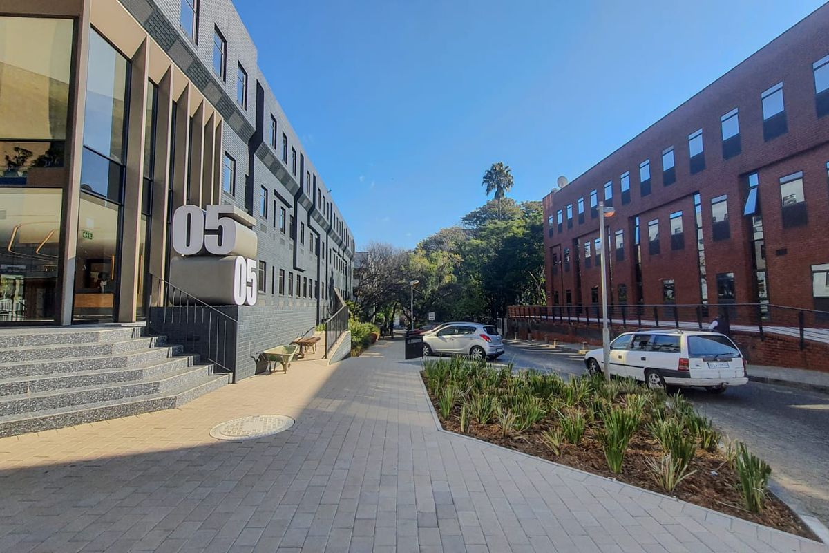 Exterior view of a modern commercial office building complex featuring paved walkways, landscaped garden beds, and a contemporary glass and brick facade.