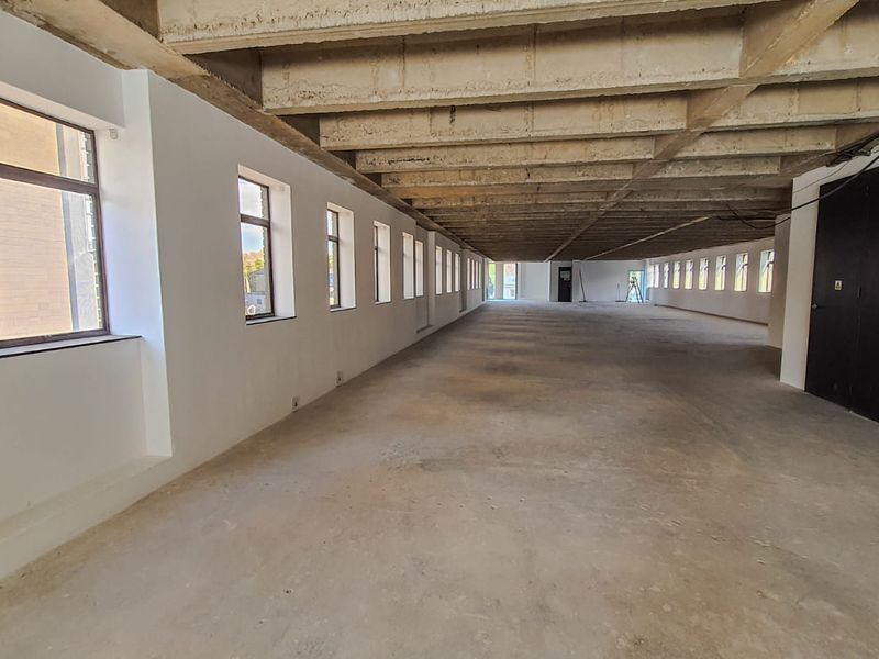 Expansive open-plan commercial space featuring an industrial aesthetic with exposed concrete ceilings, polished concrete flooring, and abundant natural light from multiple windows.
