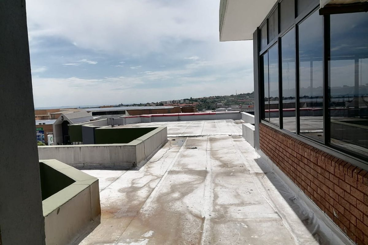 An elevated flat roof terrace area featuring brickwork and aluminium window frames, offering expansive views over the surrounding commercial property complex.