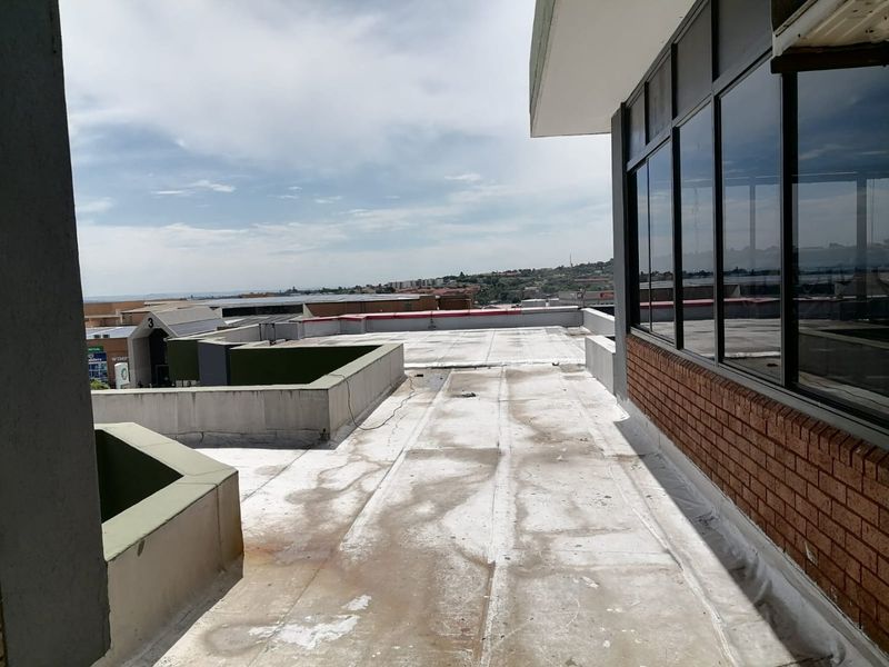 An elevated flat roof terrace area featuring brickwork and aluminium window frames, offering expansive views over the surrounding commercial property complex.