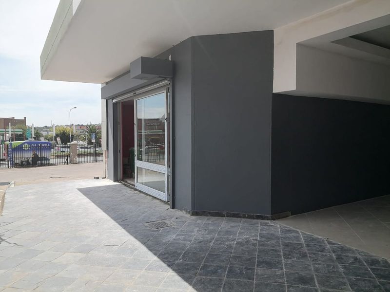 Commercial storefront entrance featuring a modern glass sliding door, dark grey facade, and tiled outdoor walkway area.