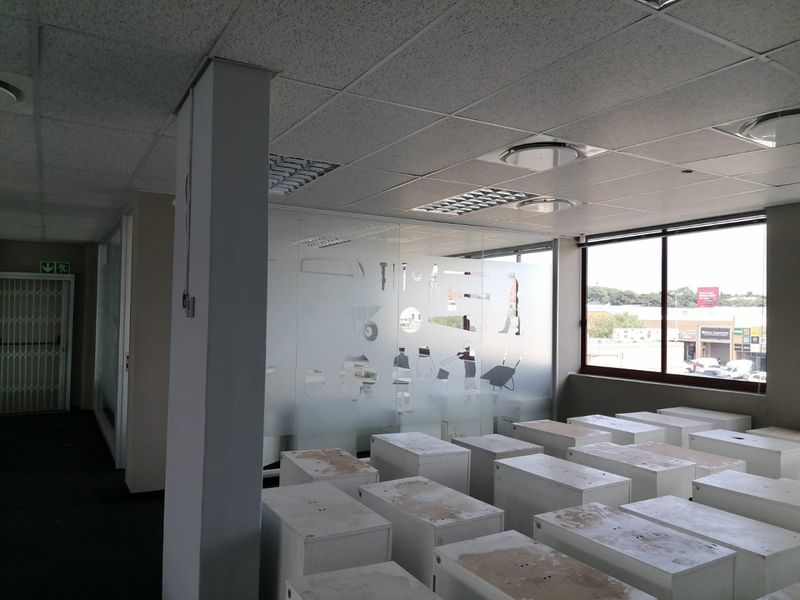 Open-plan commercial office space featuring a suspended ceiling, glass partitioning with frosted detailing, and large windows providing natural light.