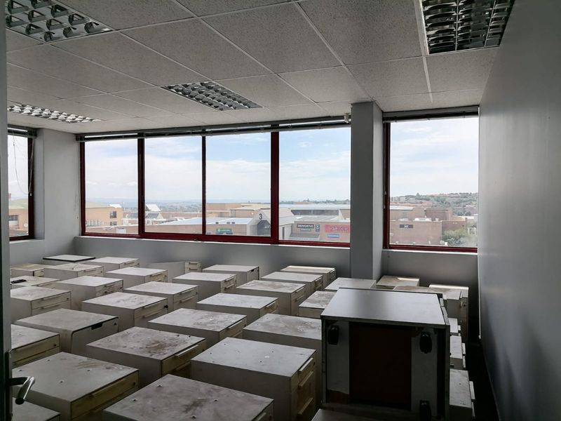 Spacious commercial office area featuring large windows with urban views, suspended ceilings, and multiple built-in storage units.