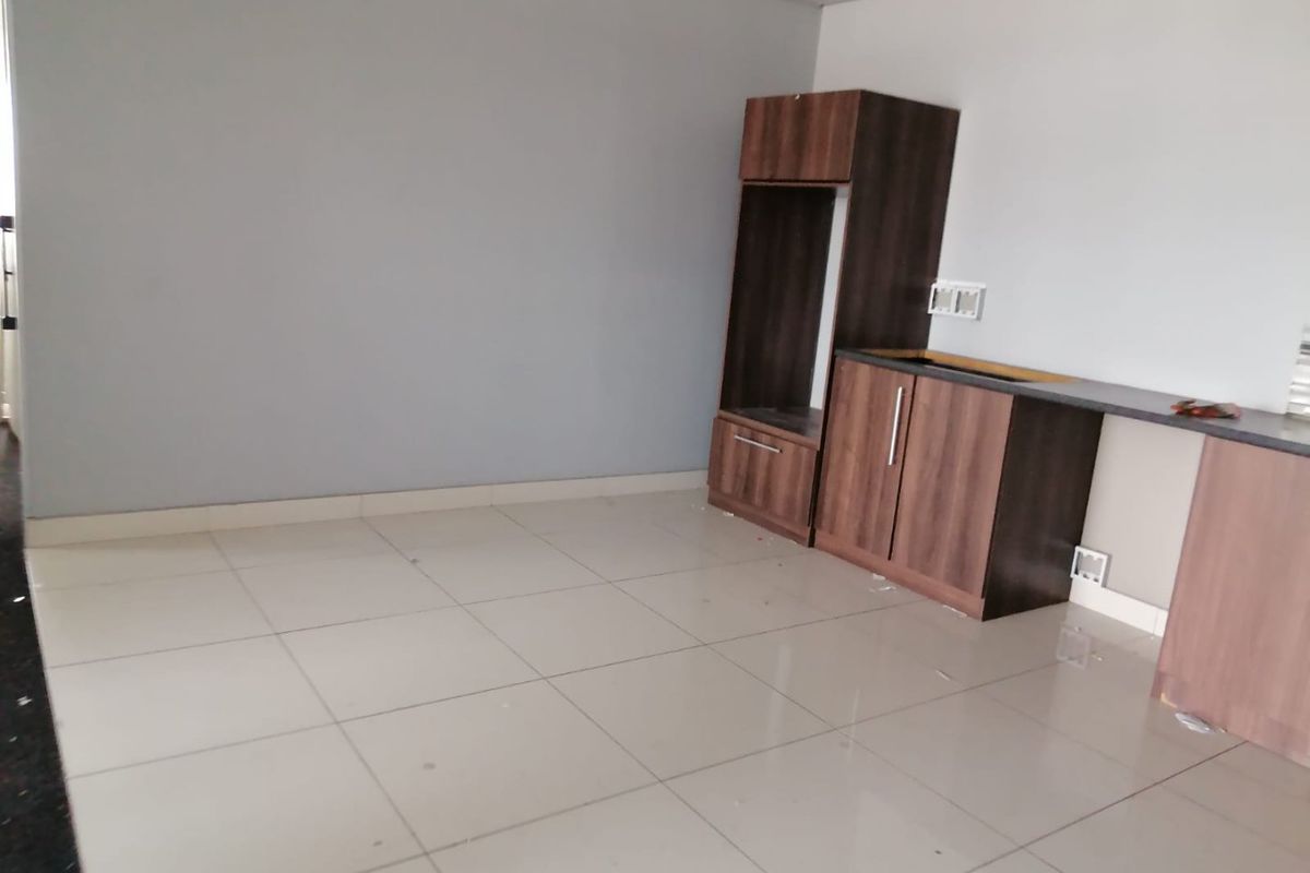 An unfinished kitchen area featuring built-in dark wood cabinetry, tiled flooring, and a countertop, currently lacking major appliances and a sink.