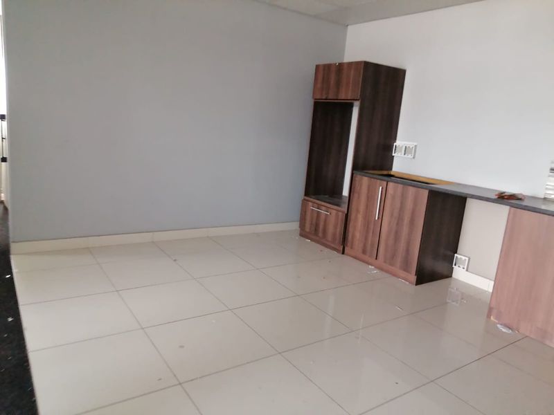 An unfinished kitchen area featuring built-in dark wood cabinetry, tiled flooring, and a countertop, currently lacking major appliances and a sink.