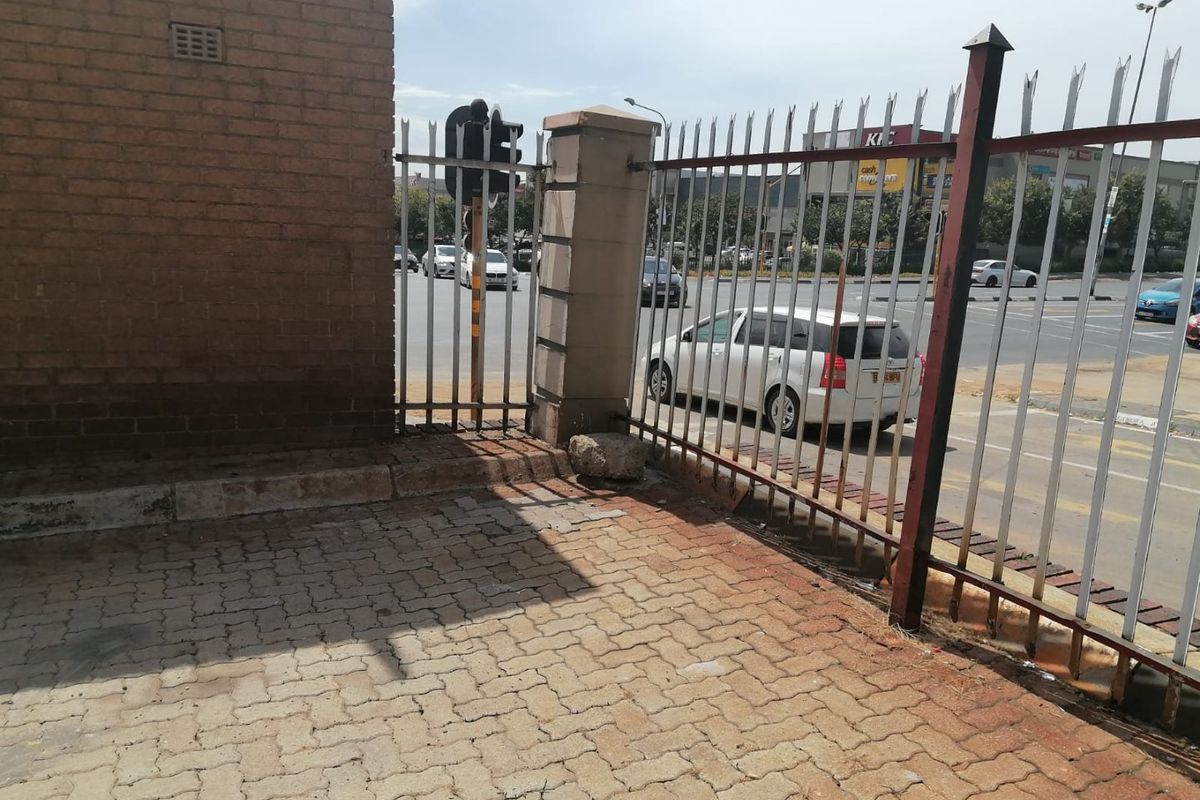 Exterior view of the property boundary featuring brick walling, metal security fencing, and paved driveway area adjacent to a busy street.