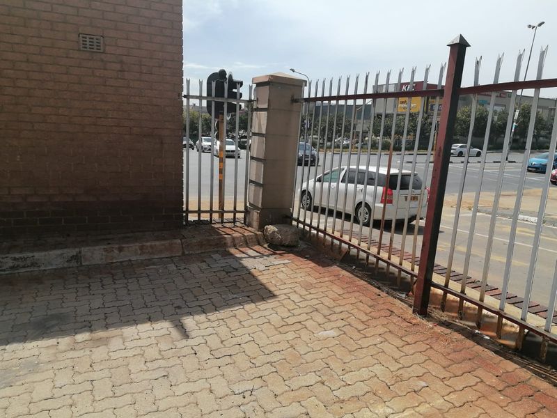 Exterior view of the property boundary featuring brick walling, metal security fencing, and paved driveway area adjacent to a busy street.