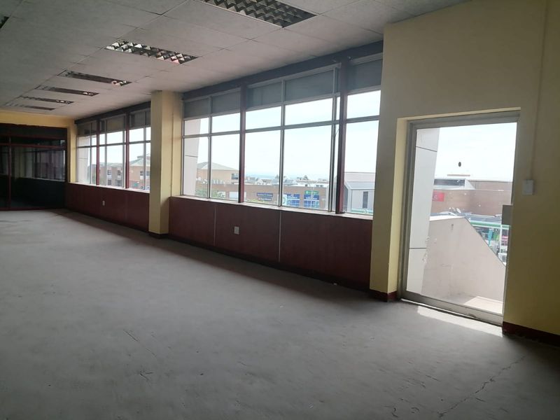 An open-plan commercial office space featuring large windows, suspended ceilings with recessed lighting, and direct access to an exterior balcony area.