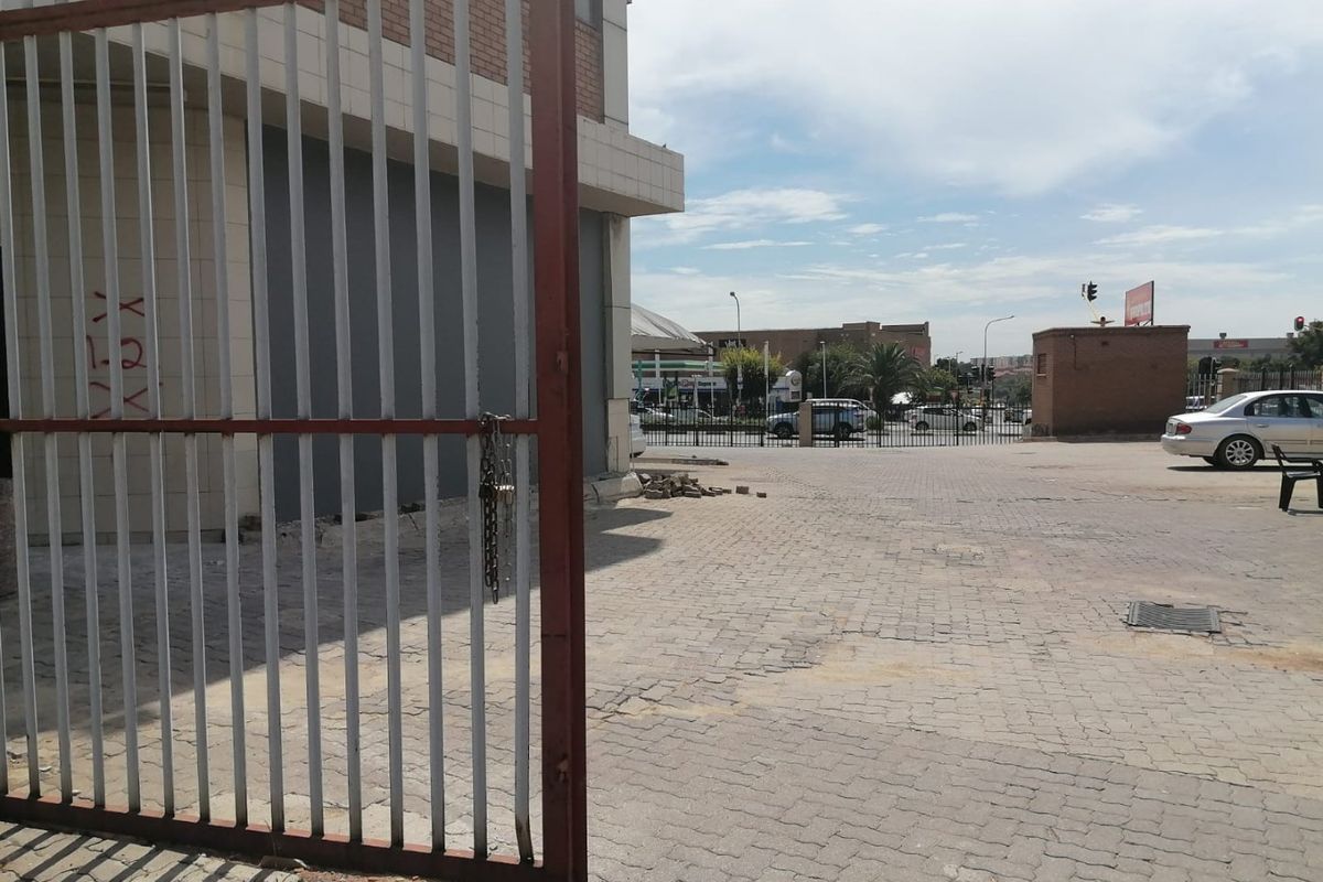 Exterior view of a commercial property featuring a paved driveway, metal security gate, and brick facade with visible signs of wear.
