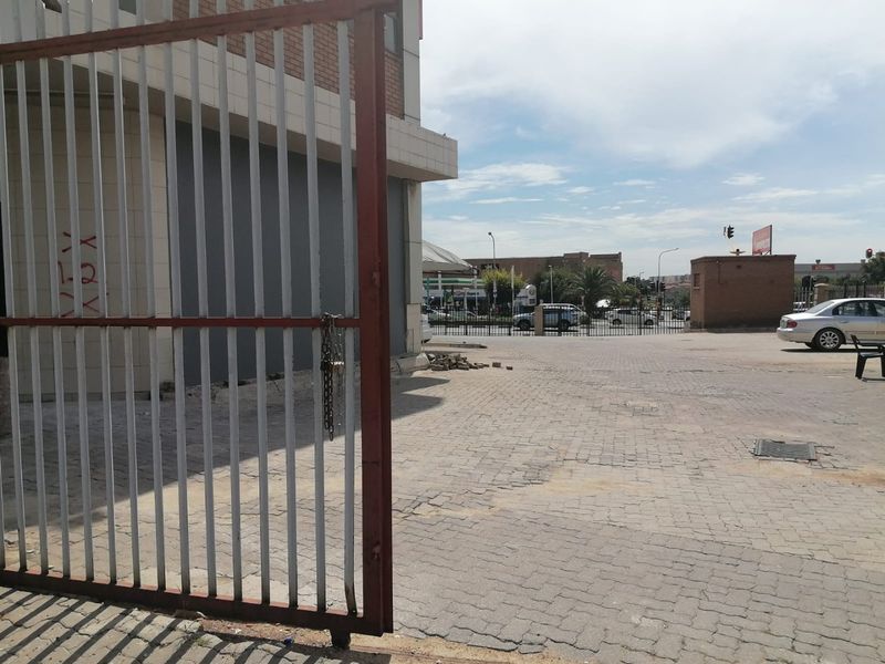 Exterior view of a commercial property featuring a paved driveway, metal security gate, and brick facade with visible signs of wear.