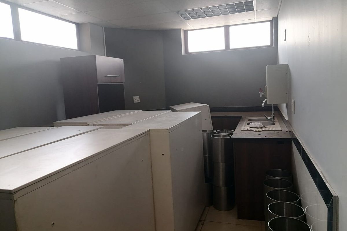 A commercial kitchen area featuring built-in cabinetry, a stainless steel sink, and tiled splashbacks, currently used for storage.