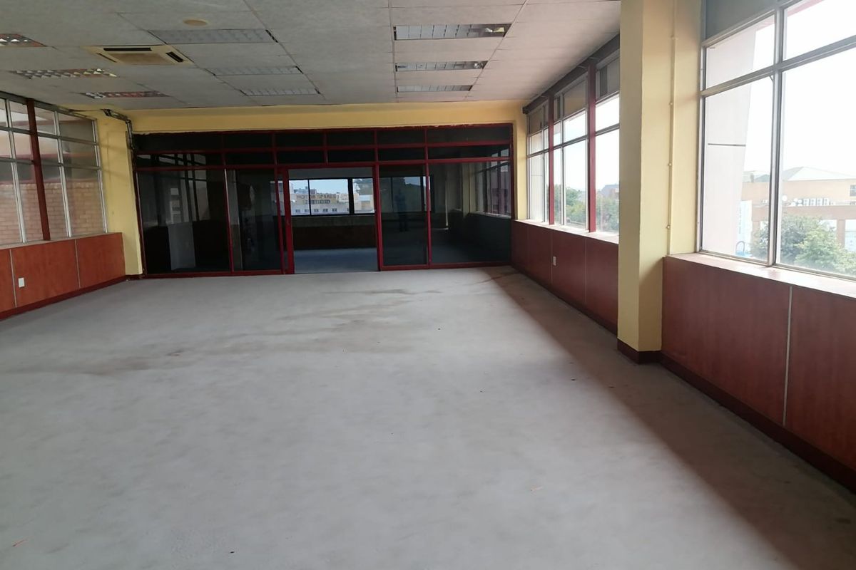 An empty, open-plan commercial office space featuring large windows, wood veneer wall paneling, and a suspended ceiling with recessed lighting.